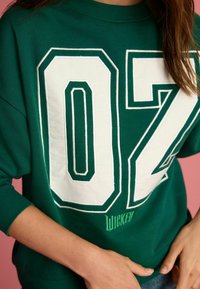 Zeleni dukserica s velikim bijelim printom "07" s kontrastnim obrubom, rebrastim manžetama i logoom "Wicked" izvezenim ispod.