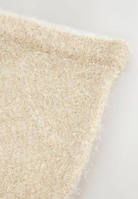 Heller beiger Stoff mit einer weichen, flauschigen Textur und schimmernden Akzenten. Die Ränder sind leicht ausgefranst, was ein einzigartiges Detail hinzufügt.