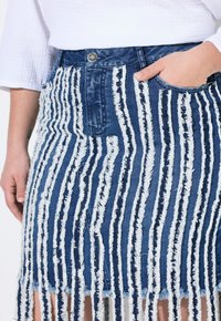 Gonna di jeans con un motivo strappato a righe blu e bianco. Presenta un'alta vita, tasca frontale e orlo grezzo.