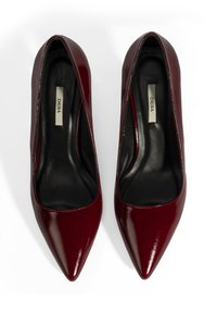 Talons hauts en cuir verni bordeaux avec un bout pointu et une finition lisse et brillante. L'intérieur est doté d'une doublure noire et d'un logo embouti.