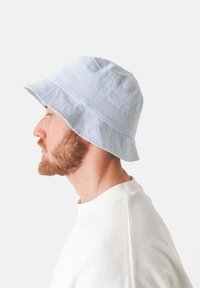 Jasnoniebieski bawełniany kapelusz typu bucket z szerokim rondem i teksturowanym materiałem, pokazany z boku na osobie w białej bluzce.