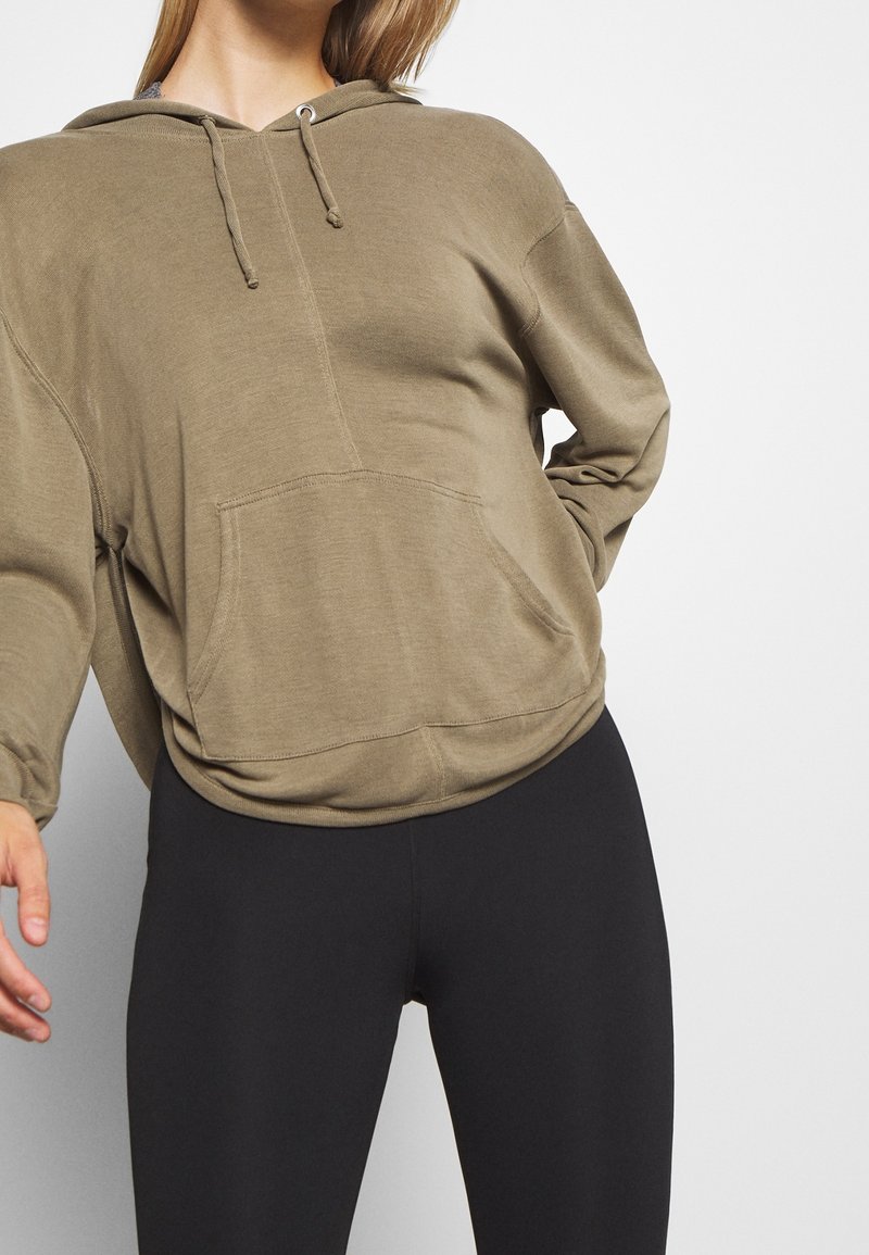 Olivgrön huvtröja i mjukt tyg, med en framficka som är en känguruficka och en dragsko för huvan. Kombinerad med svarta leggings.