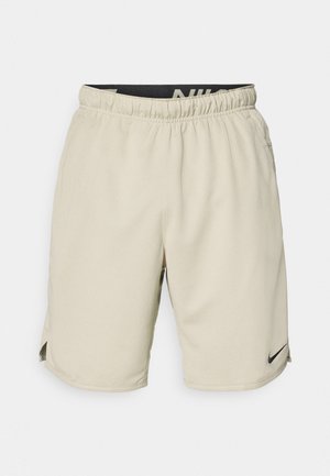 Beige athletic shorts made from lightweight fabric, featuring an elastic waistband, side slits, and a small black Nike logo on the lower left side.