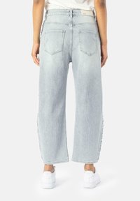Jeans in un leggero blu, a gamba larga, con cuciture laterali sfilacciate e due tasche posteriori. Abbinati a sneakers bianche, sottolineando un look casual.