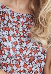 Haut en tissu à imprimé floral présentant de petites fleurs rouges et bleu clair sur un fond sombre. Texture lisse avec un décolleté échancré et une coupe décontractée.