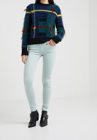 Vervaagde blauwe en groene geblokte sweater met rode en gele accenten, gecombineerd met lichte mintkleurige skinny jeans en zwarte enkellaarsjes met een gesp.
