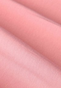 Lichtroze stof met een gladde textuur en een subtiele ribbelstructuur. Vouwlagen tonen de drapeerkwaliteit van de stof en de uniforme kleur.