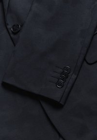 Blazer azul marino con un patrón sutil, tejido suave, forma estructurada y cuatro botones negros en el puño con costura decorativa.