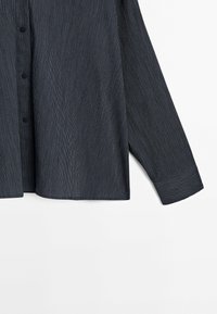 Manche et partie basse avant d'une chemise gris foncé à fines rayures avec boutons, sur fond blanc