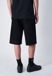 Zwarte knie-lange shorts gemaakt van lichtgewicht stof, met een relaxte fit en zonder zichtbare logo's. Draag het met zwarte sokken en sneakers.
