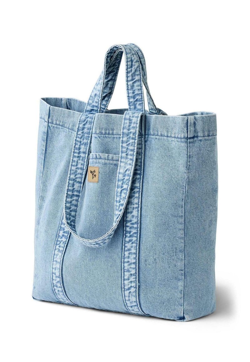 Sac en denim bleu clair avec deux poignées robustes, des coutures verticales et une petite étiquette sur la poche avant. Texture douce. Forme rectangulaire.