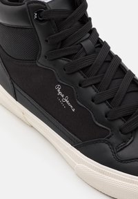 Black high-top sneaker with a leather and mesh upper, featuring black laces, a white outsole, and a small printed logo on the side.