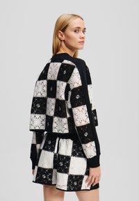 Zwart-witte cropped top met een ruitjespatroon, versierd met kanten details en geribbelde manchetten, gecombineerd met een bijpassende rok.