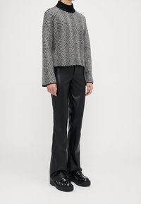 Černobílý svetr s herringbone vzorem a vysokým límcem, spárovaný s kalhotami vysokého pasu z černé umělé kůže a robustními platformovými botami.