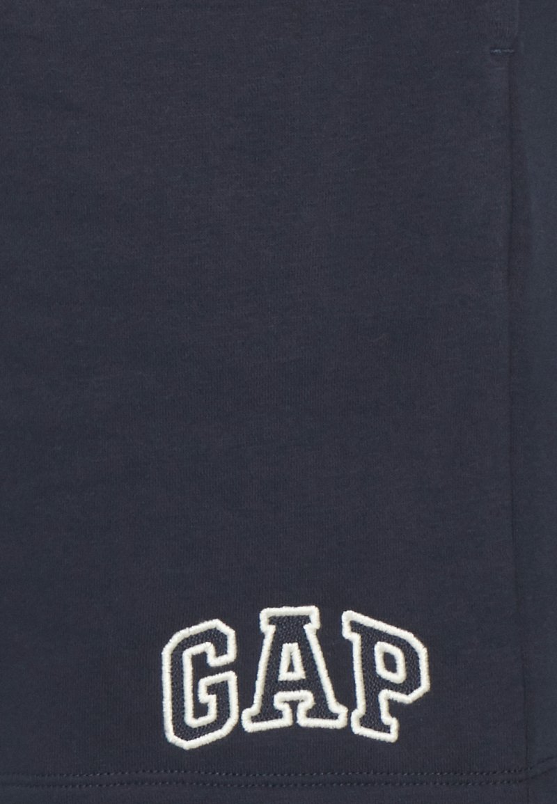 Marineblaue Baumwoll-T-Shirt mit weißem, gesticktem "GAP"-Logo in der unteren linken Ecke, mit einer glatten Textur und kurzen Ärmeln.