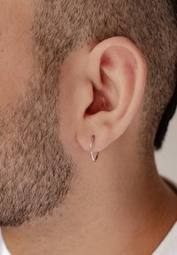 Boucle d'oreille en argent dans une oreille percée ; gros plan montrant la texture des cheveux et le teint de la peau. Design minimaliste avec une finition polie.