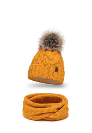 Gehaakte gele beanie met een nepbont pompon bovenop, met een gevlochten patroon en geribbelde manchet. Vergezeld van een bijpassende gele infinity-sjaal.