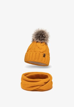 Gehaakte gele beanie met een nepbont pompon bovenop, met een gevlochten patroon en geribbelde manchet. Vergezeld van een bijpassende gele infinity-sjaal.