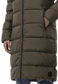 Duga, pahuljasta parka u maslinasto zelenoj boji, s dugim zatvaračem, bočnim džepovima i dušekom s kviltanim uzorkom s horizontalnim šavovima.
