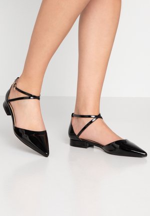 Sorte laklæder flade sko med spids tå, ankelremme og lav blokhæl. Glat tekstur og skinnende finish. Minimalistisk design.