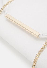 Valkoinen tekonahkainen clutch-laukku, jossa on kultainen suorakaiteen muotoinen metallikoriste ja kultainen metalliketjuhihna, sileällä tekstuurilla.