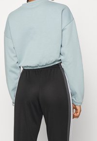 Felpa azzurra chiara con scollatura arrotondata e orlo elasticizzato, abbinata a pantaloni joggers neri con strisce laterali bianche. Tessuto morbido.