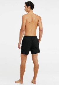 Zwarte zwembroek met een elastische tailleband, zijzakken en een gladde textuur, getoond op een mannenfiguur van achteren.