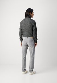 Pulover gri tricotat cu guler înalt, asociat cu pantaloni tapered gri deschis. Caracteristici notabile includ un tricot cu textură și manșete ajustabile.