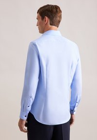 Camicia a maniche lunghe azzurro chiaro con texture liscia, colletto standard, polsini con bottoni e fondo arrotondato. Vestibilità sartoriale, mostrata da dietro.