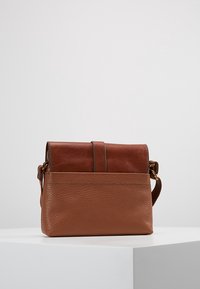 Brązowa skórzana torebka na ramię z teksturowaną dolną częścią, gładką klapą i regulowanym paskiem, umieszczona na białej powierzchni na jednolitym tle.