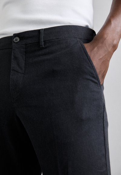 Svarta byxor med slim fit, tillverkade av ett texturerat tyg. Har en framficka, knappstängning och bältesöglor.