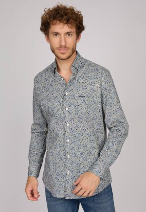 Chemise boutonnée en tissu léger, présentant un motif floral bleu sur fond crème, avec un col classique et des manches longues.