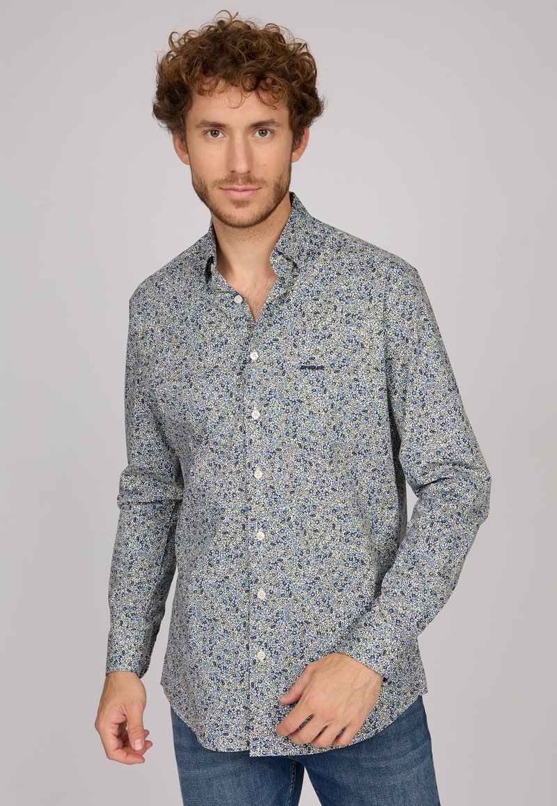 Chemise boutonnée en tissu léger, présentant un motif floral bleu sur fond crème, avec un col classique et des manches longues.