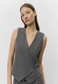 Gray, sleeveless wrap top made of a soft fabric. Features a deep V-neck and a single button accent at the hem. Clean, minimalist design.
