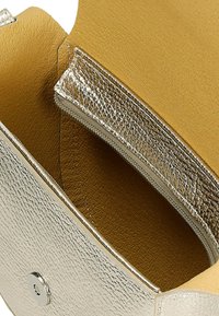 Interieur van een metallic zilveren handtas met een gestructureerde afwerking, met een ritscompartiment en een zachte gele voering.