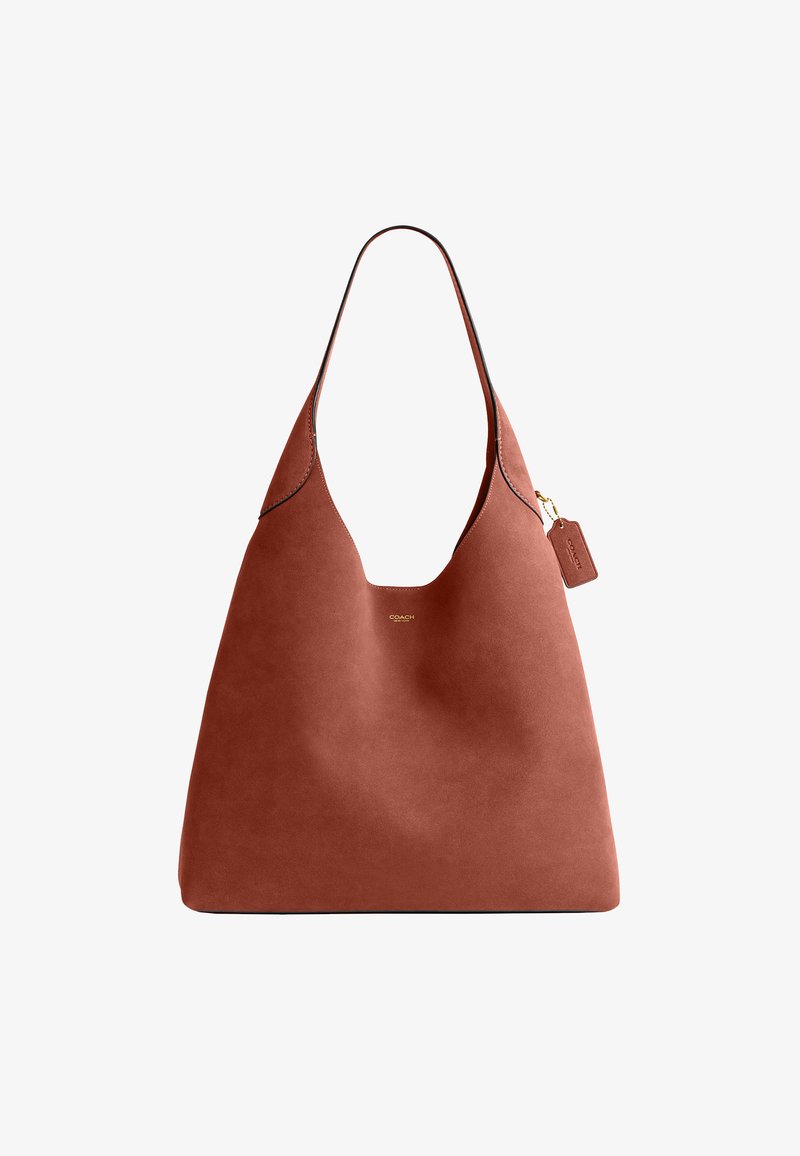 Sac cabas en cuir marron avec une seule bandoulière et une petite étiquette attachée avec un marquage en relief.