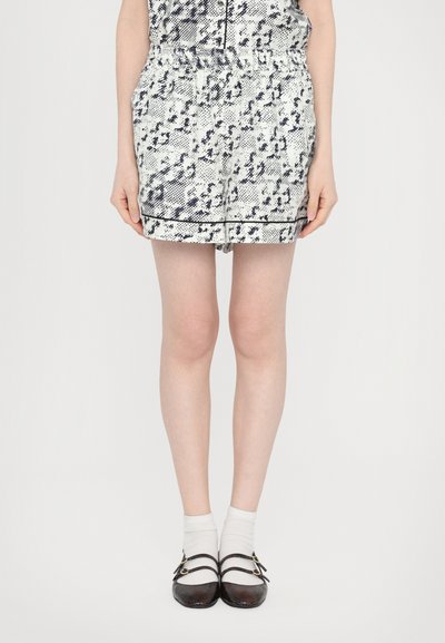 Weiß und marineblaue gemusterte Shorts mit einem elastischen Bund, die vordere Taschen und einen schwarzen Akzent am Saum haben. Getragen mit schwarzen Schuhen und weißen Socken.
