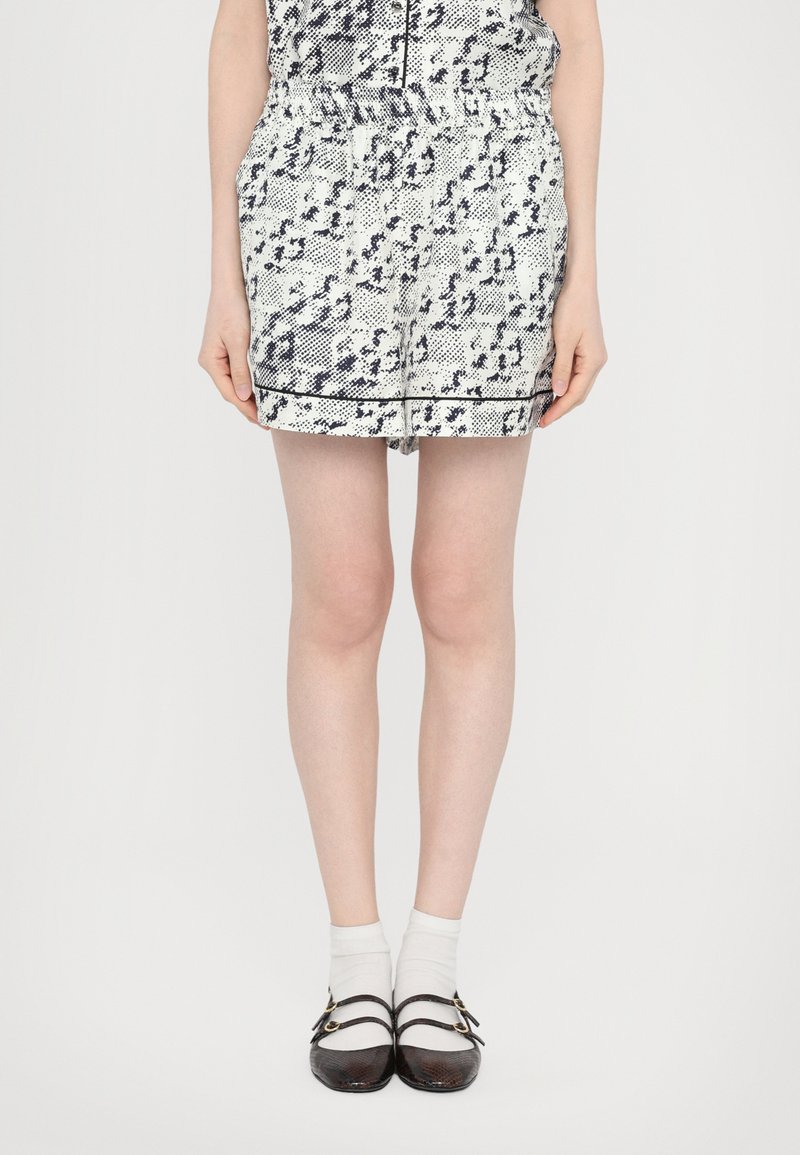 Shorts alb și bleumarin cu model, cu talie elastică, având buzunare frontale și un accent negru la tiv. Purtați cu pantofi negri și șosete albe.