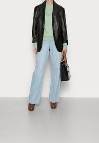 Svart läderblazer, grön sweatshirt, ljusblå vida jeans, bruna plattformsskor och en svart handväska med brunt handtag.