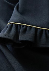 Tissu noir avec un bord ondulé présentant une fine bordure dorée. Texture lisse avec un éclat subtil, mettant en valeur le design en couches.