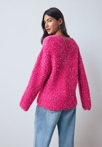 Luchtige roze trui gemaakt van gestructureerd garen met metalen draadjes, met een losse pasvorm, brede mouwen en een ronde halslijn, gecombineerd met lichtblauwe spijkerbroek.