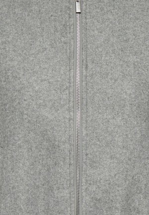 Primer plano de una tela de forro polar gris con una cremallera metálica plateada vertical centrada y completamente cerrada.