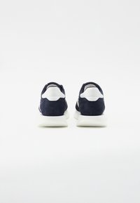 Baskets en suède bleu marine avec des accents blancs, dotées d'une semelle rembourrée et d'un bout rond. Le design inclut un talon texturé et une finition lisse.