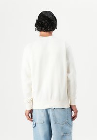 Felpa bianca a girocollo realizzata in tessuto morbido, con polsini e orlo a coste, indossata con jeans cargo blu chiaro. Design minimalista.