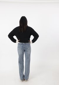 Suéter corto negro de punto con dobladillos acanalados, combinado con jeans de pierna recta de tiro alto en azul claro, que cuentan con bolsillos traseros y costuras.