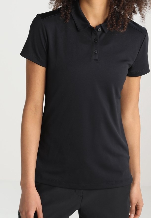 Personne portant un polo noir à manches courtes et un pantalon noir, debout devant un fond clair, visible des épaules aux hanches.