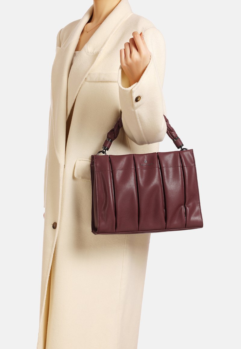 Borsa a mano in pelle malva con design plissettato, struttura solida e manico intrecciato, tenuta da una persona in un cappotto color crema.