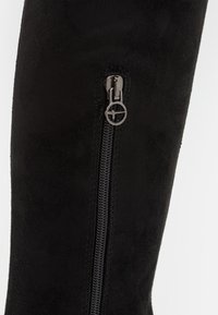 Černé semišové nadkolenní boty s bočním zipem a kulatým táhlem, hladkým povrchem a bez viditelného kovového materiálu kromě zipu.