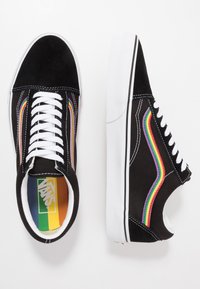 Sorte mockasin-sneakers med et flerfarget bølgedesign på sidene, hvite snører og en gummisåle med svart og hvite detaljer.