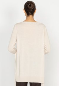 Długi beżowy kardigan wykonany z miękkiej dzianiny. Posiada luźny krój, ribbowe wykończenie u dołu oraz boczne rozcięcia dla swobody ruchów.